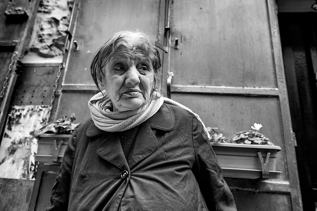 A woman wearing a scarf on a street of stone buildings.